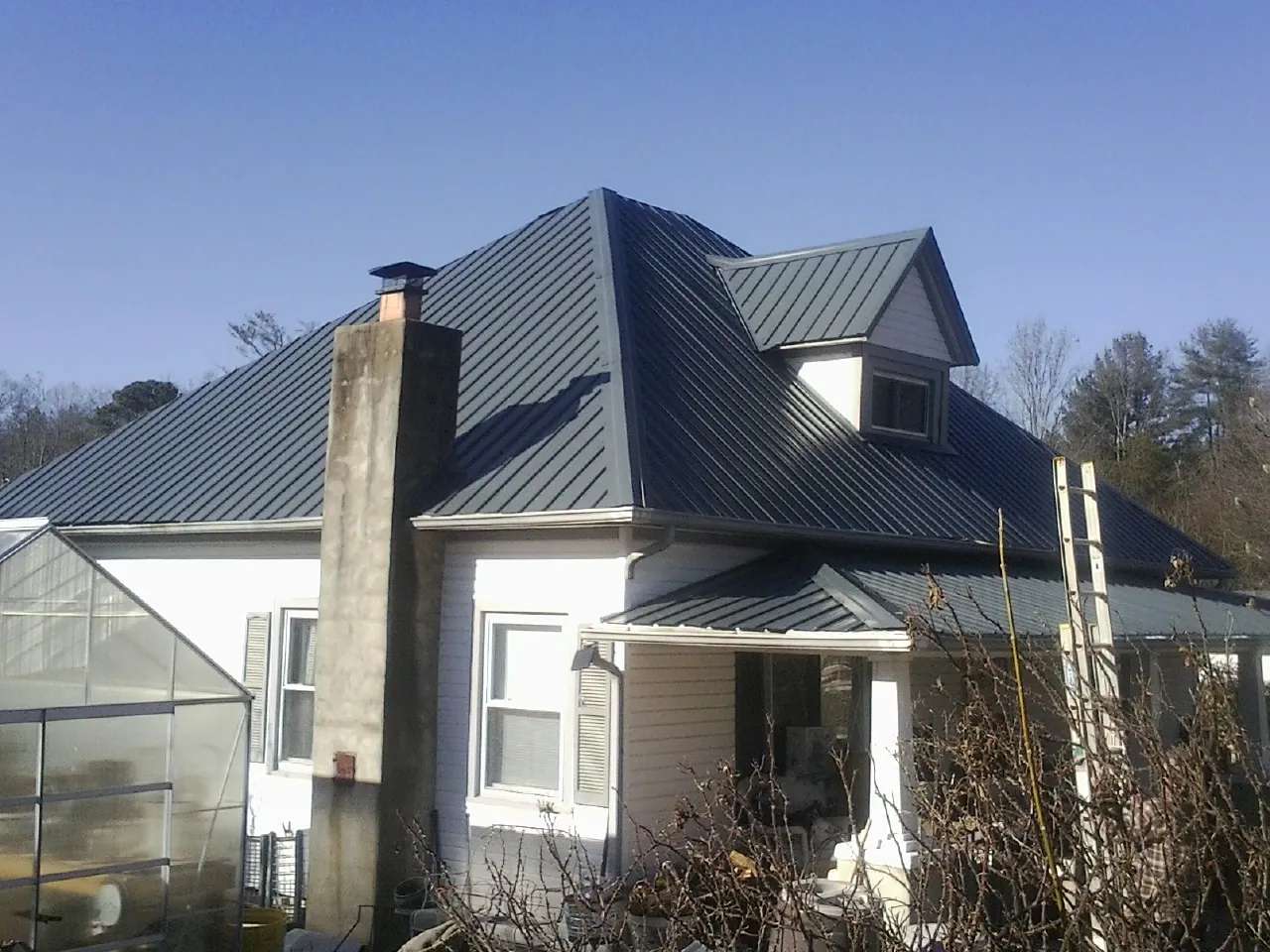Dark blue standing seam metal roof on a white farmhouse with dormer — Slate & Tile Roof Repair by Roofing Brothers in Mckinney