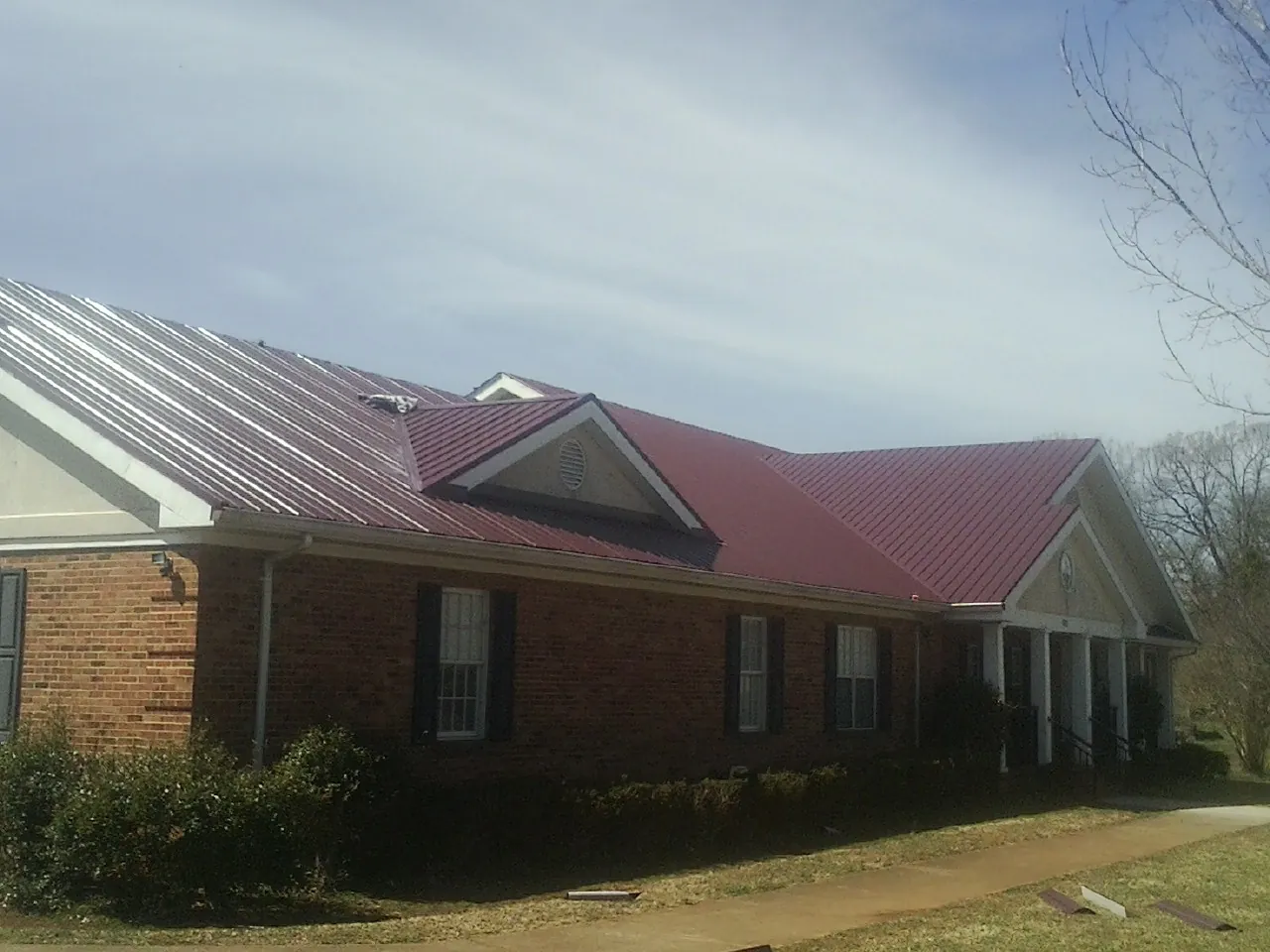 Red metal roof with gabled entries on a long brick building, from a Hail Damage Roof Repair job in Mckinney