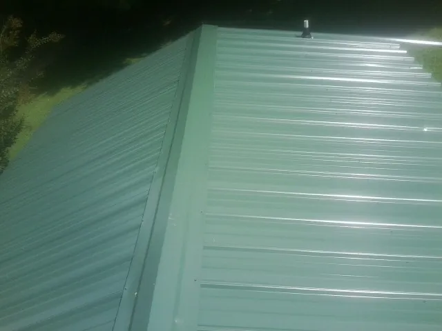New green metal panels meeting at the ridge of a roof — Flat Roof Repair work by our crew in Mckinney