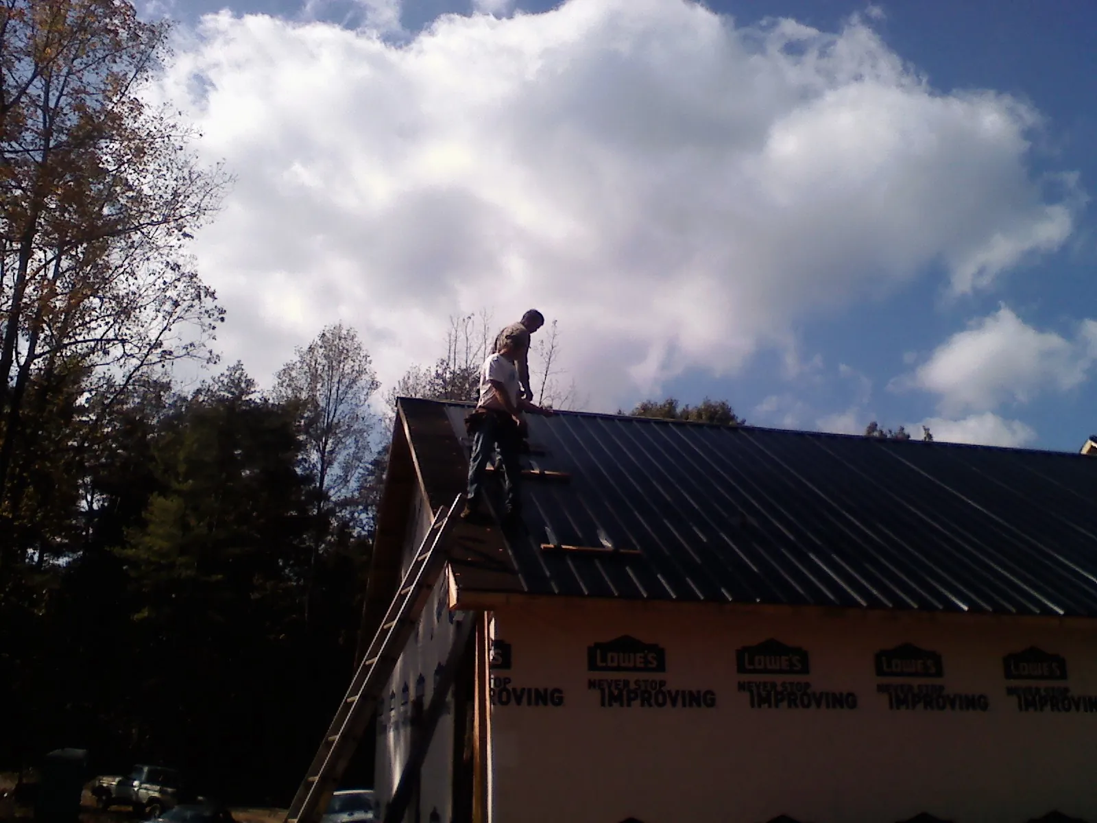Roofer fastening dark metal panels high against a cloudy sky, from a Roof Inspection job in Mckinney