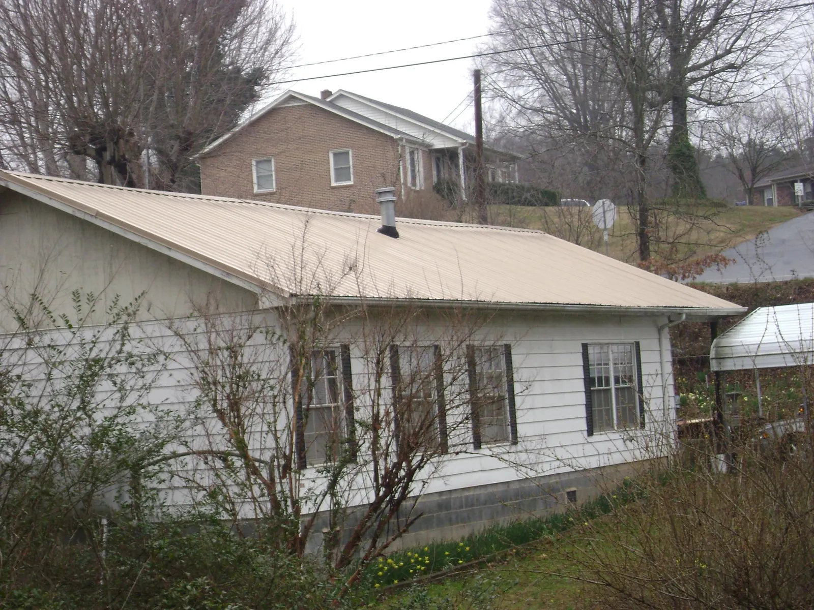 Tan metal roof on a white sided house set into a hillside — Commercial Roofing by Roofing Brothers in Mckinney